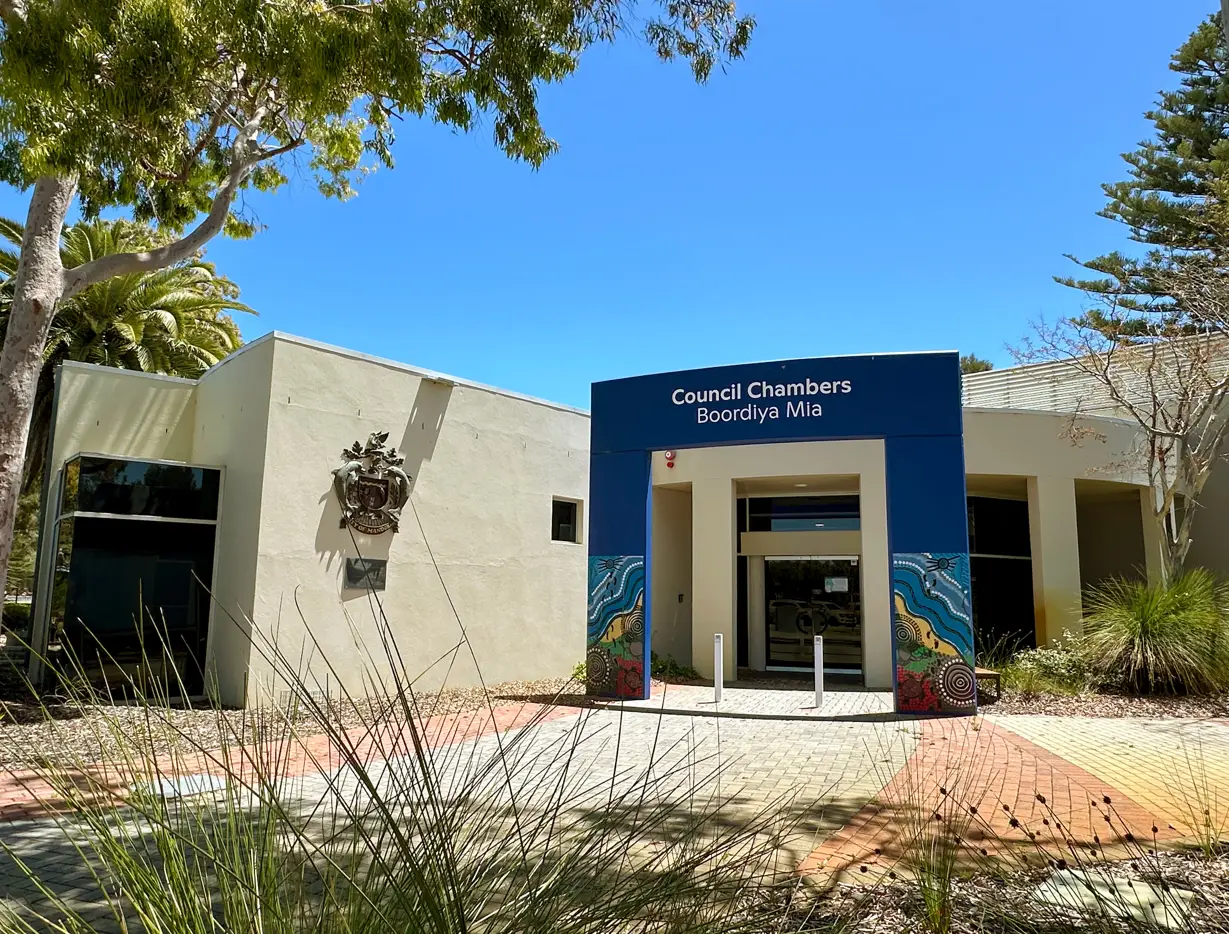 Front entrance of Mandurah Council Chambers (Boordiya Mia) surrounded by native landscaping, under a blue sky.